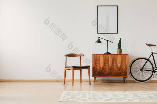 时尚的椅子旁边的复古橱柜和复古自行车在斯堪的纳维亚最小的内饰, 真正的照片与复制空间墙上
