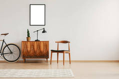 时尚的椅子旁边的复古橱柜和复古自行车在斯堪的纳维亚最小内饰与模型在墙上和地毯上的木地板上, 真实的照片与复制空间在墙上