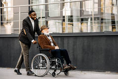 快乐的高级残疾人在轮椅和非洲裔美国人 cuidador 骑在街上