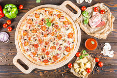 大比萨饼与培根, 蘑菇和西红柿在一个圆形的切菜板上的一个黑暗的木制背景。食品配料.