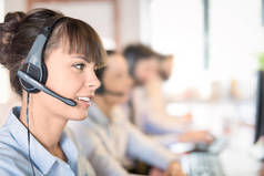 呼叫中心工作人员在她的团队的陪同下。微笑的客户支持操作员在工作。使用耳机的年轻员工.