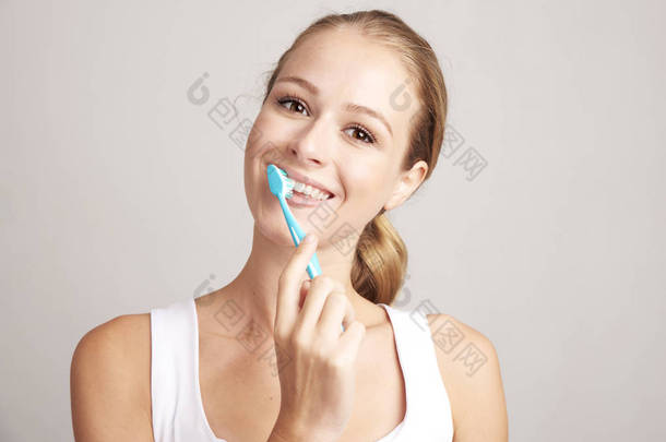 工作室拍摄美丽的年轻女子刷牙, 同时看着相机和微笑。隔离在<strong>浅灰色背景</strong>上.