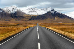 在一个多云的秋日, 冰岛高耸的白雪覆盖的山脉的空旷道路
