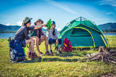 一群年轻的亚洲朋友在湖边享受野餐和聚会, 他们背着野营背包和椅子。年轻人敬酒和欢呼的啤酒瓶。人和生活方式的概念。户外背景主题