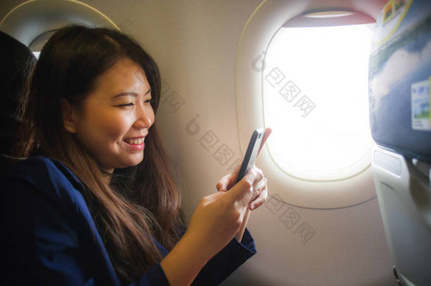 年轻快乐和美丽的亚洲韩国妇女在飞机机舱内出差的生活方式肖像微笑愉快使用手机在<strong>无线上网</strong>和互联网上飞行的概念