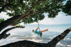 一个年轻的女人在海边的一棵大树的树荫下荡秋千。海滩上的女孩在热带岛屿的海岸上荡秋千.