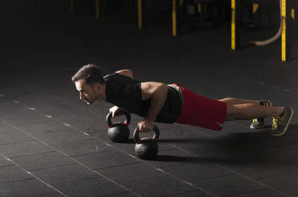 运动员在健身房的壶铃上锻炼俯卧撑。带有复制空间的黑暗摄影概念.
