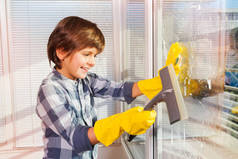 戴着海绵和玻璃雨刷的防护手套清洁窗户的小男孩肖像