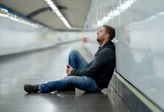 悲伤的年轻人哭着遭受抑郁压力坐在地面街道地铁隧道看起来绝望独自靠在墙上精神障碍情绪痛苦成瘾和失业的概念.
