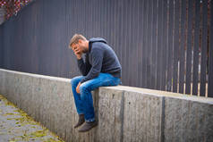 患有抑郁症的年轻有魅力的男人独自坐在大街上, 在失业中感到焦虑和孤独的年轻的有魅力的男人.