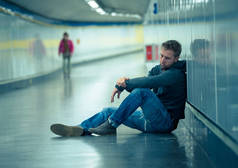 悲伤的年轻人哭着遭受抑郁压力坐在地面街道地铁隧道看起来绝望独自靠在墙上精神障碍情绪痛苦成瘾和失业的概念.