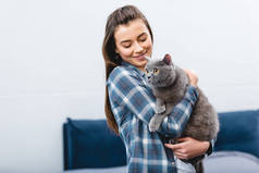 微笑的年轻女子抱着可爱的英国短猫