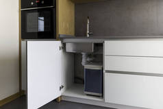 打开厨柜, 配有水槽和安装垃圾桶, 智能解决方案为厨房设计。厨房采用现代阁楼风格, 提供白色、灰色和木质的细节.