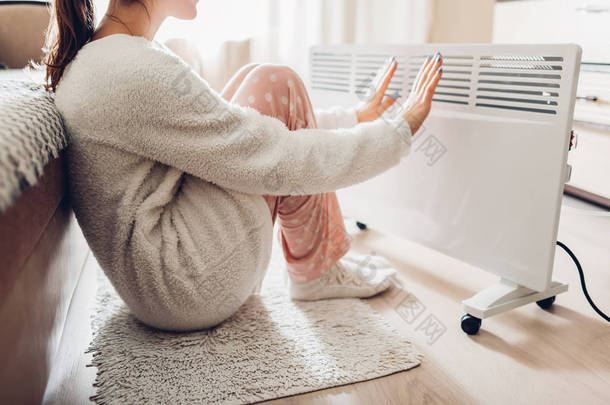 冬天在家使用加热器。妇女<strong>温暖</strong>她的手坐在设备和穿着<strong>温暖</strong>的衣服。加热季节.