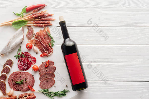 在白色木制桌面上的<strong>红酒瓶</strong>和各种肉类小吃的顶部视图