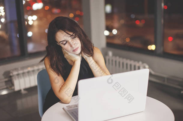 晚上在办公室里拿着笔记本电脑在桌旁工作的女商人。窗外是<strong>点亮</strong>的五颜六色的<strong>灯光</strong>。截止日期, 加班.
