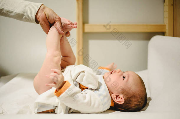 母亲给婴儿换尿布, 抬起小腿.
