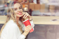 女人坐在咖啡厅里喝她的热咖啡。时尚的微笑的女人在冬季衣服的肖像喝热咖啡。女性冬季风格。-图片仅供参考