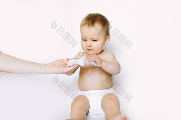 卫生-年轻的妈妈用湿巾擦拭婴儿皮肤。小女婴穿着尿布坐着, 拿着妈妈手上的湿擦。清洁擦拭, 纯净, 清洁