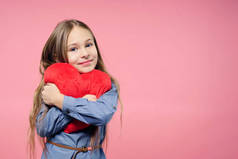 爱的概念。可爱的孩子女孩拿着红色的心脏在粉红色的背景。情人节。母亲节.