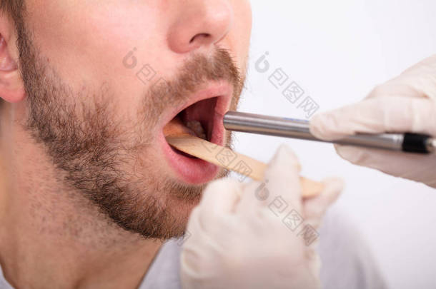 医生用舌抑制剂对人的喉咙进行手部检查的特写