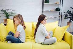 愤怒和疯狂的女孩坐在房间里的黄色沙发上。他们不看对方。女孩们都很难过.