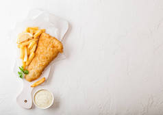 传统的英国鱼和芯片与塔塔酱在切菜板上白色桌子背景.