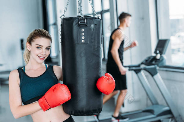 有吸引力的运动女孩在拳击手套举行打气筒和微笑在健身房的相机