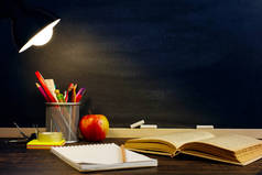 晚上, 老师的桌子或工人, 写作材料就在上面, 一本书和一个苹果, 在灯下。学校主题的文本或背景为空白。复制空间.