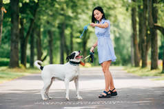 愉快的年轻女子在蓝色礼服与大黑白狗在夏季公园