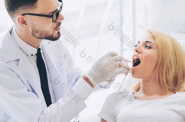 年轻英俊的牙医检查在牙科诊所坐在牙医椅上的快乐妇女病人的牙齿。牙科护理概念.