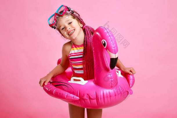 愉快的女孩在泳装与游泳圈火烈鸟在一个有色的粉红色的背景