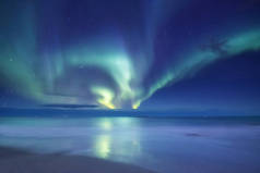 挪威洛福敦群岛上的北极光。海洋上方的绿色北极光。夜晚的天空与极光。夜间冬季景观与极光和反射的水面上。诺威形象