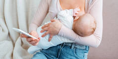 年轻母亲母乳喂养婴儿的裁剪镜头, 并使用智能手机