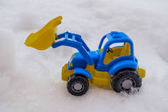塑料蓝色和黄色玩具拖拉机与前装载机在雪中。公用事业和除雪的概念。道路服务.