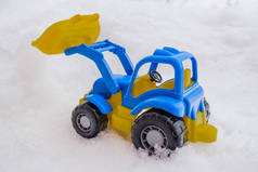 塑料蓝色和黄色玩具拖拉机与前装载机在雪中。公用事业和除雪的概念。道路服务.