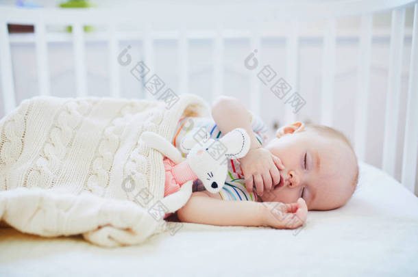 可爱的女婴睡在共睡<strong>婴儿床</strong>连接到父母的<strong>床</strong>与填充玩具。小孩在<strong>婴儿床</strong>上小睡了一天。睡眠训练理念。阳光明媚的托儿所里的小孩