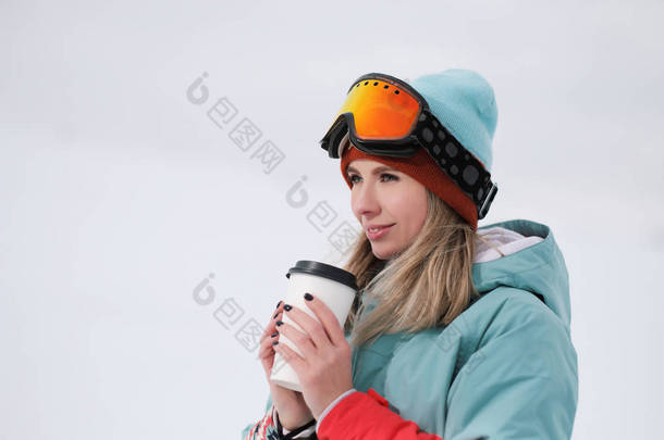 一个穿着极限运动服、帽子和头盔、戴着口罩的美丽的年轻咀嚼女子拿着一个<strong>纸杯</strong>, 手里拿着热咖啡<strong>饮料</strong>.