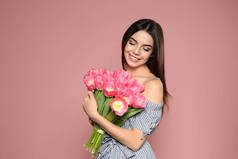 美丽的微笑的女孩的画像与春天郁金香在粉红色背景。国际妇女节