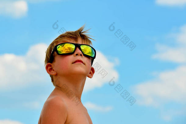 一个小男孩戴着眼镜望着多云的天空。云反映在玻璃上。黄色的太阳对蓝天.