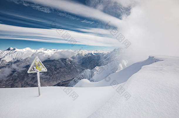 黄色危险标志, 冬天的山, 蓝天和雪暴风雪来背景