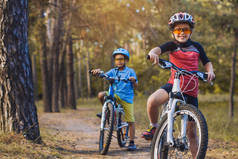 孩子们在阳光明媚的森林里骑着自行车. 快乐的孩子们戴着头盔在户外骑车