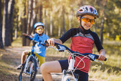 孩子们在阳光明媚的森林里骑着自行车. 快乐的孩子们戴着头盔在户外骑车