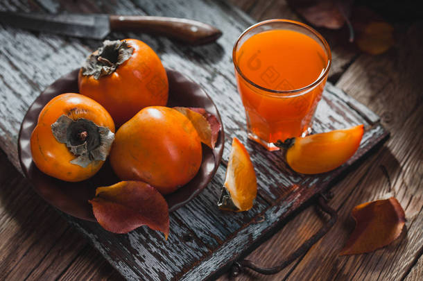 一杯新鲜果汁和成熟的橙汁和叶, 放在棕色木桌上的棕色盘子里。新鲜水果