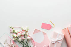 粉红色的 eustoma, 纸卷, 包裹的礼物, 信封, 标签和贺卡在灰色背景上的顶部视图