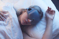 睡觉的女孩在一个与夜间照明的矫形枕头上的睡眠面具, 白色床单.