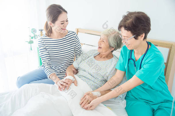 医生与快乐的老年女患者交谈, 与家人躺在床上