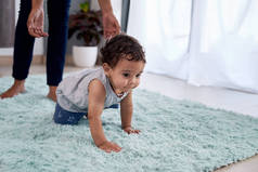 男婴爬行地毯与母亲父母在背景帮助