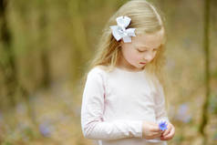 可爱的小女孩采摘春天的第一朵花在树林里, 在美丽的阳光明媚的春日。可爱的孩子有乐趣户外.
