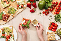 妇女拿着一杯咖啡在餐桌上与成分, 绿色和烤面包与蔬菜和西葫芦的顶部视图